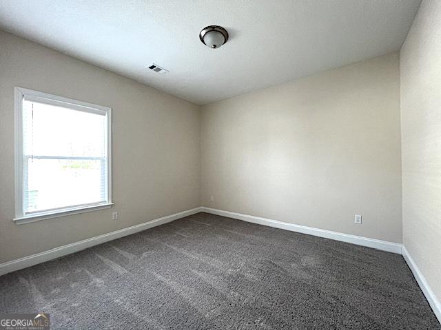 empty room featuring visible vents, baseboards, and dark colored carpet