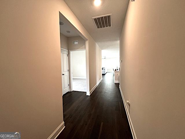 hallway with visible vents, baseboards, and dark wood-style flooring