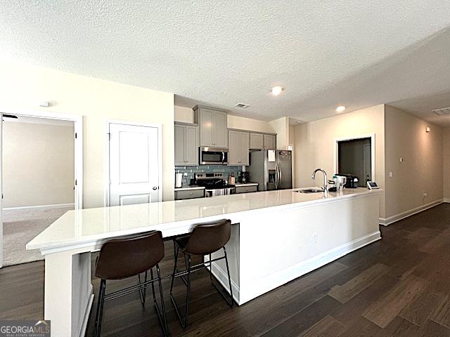 kitchen with dark wood finished floors, light countertops, gray cabinets, appliances with stainless steel finishes, and a sink