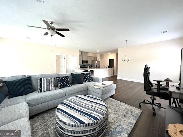 living room featuring a textured ceiling, ceiling fan with notable chandelier, dark wood-style flooring, and baseboards