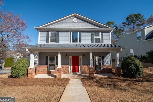 view of front of house with a standing seam roof, a porch, brick siding, and metal roof