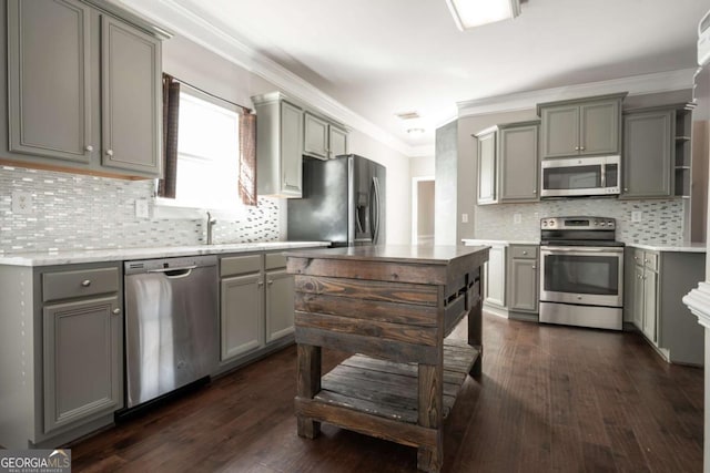 kitchen featuring gray cabinetry, ornamental molding, tasteful backsplash, dark wood-style floors, and appliances with stainless steel finishes