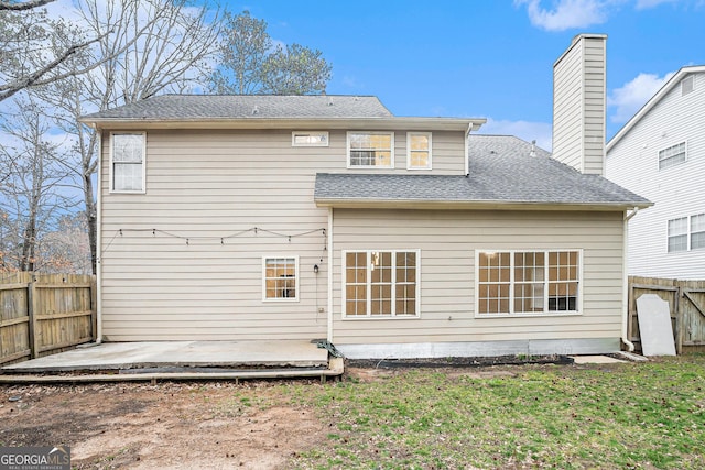 rear view of property featuring fence, roof with shingles, a lawn, a chimney, and a patio area