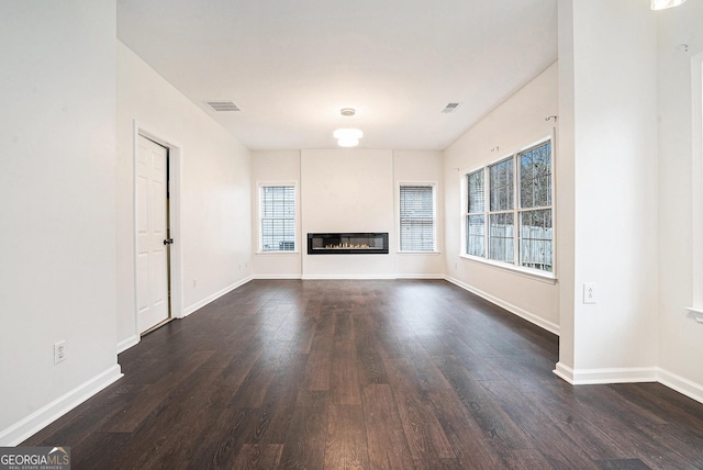 unfurnished living room featuring a glass covered fireplace, dark wood-type flooring, baseboards, and visible vents