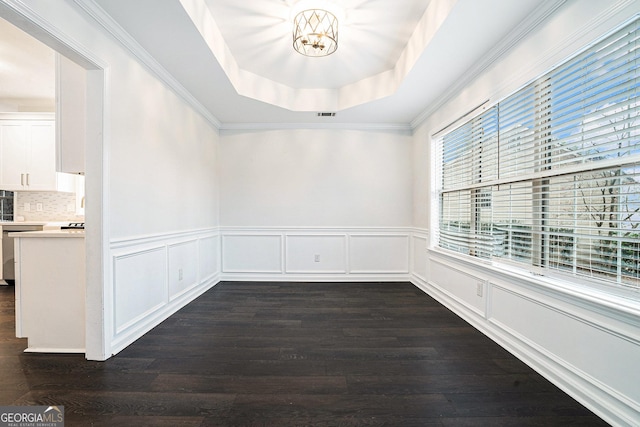 spare room with a wainscoted wall, a raised ceiling, a notable chandelier, and dark wood-type flooring