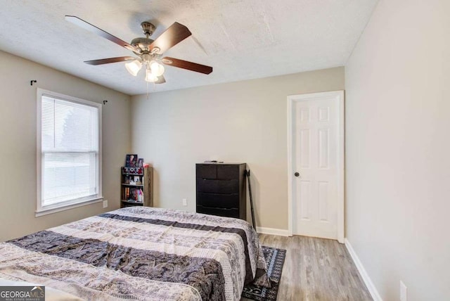 bedroom with a ceiling fan, wood finished floors, baseboards, and a textured ceiling