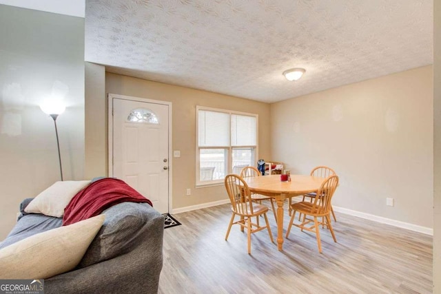 dining area featuring light wood-type flooring, baseboards, and a textured ceiling