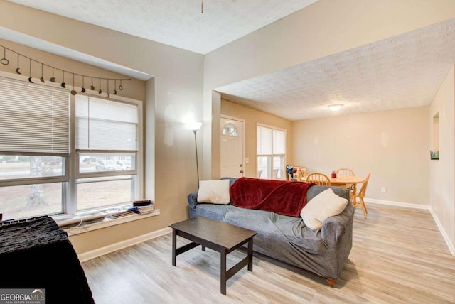 living room with baseboards, a textured ceiling, and light wood finished floors