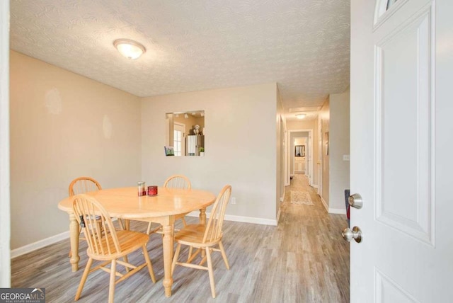 dining room featuring baseboards, light wood-type flooring, and a textured ceiling