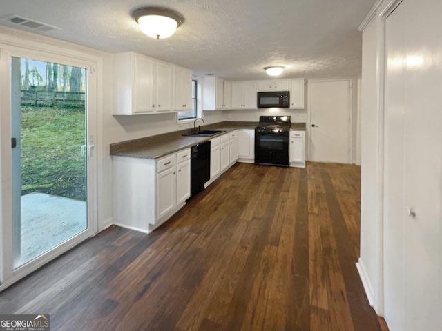 kitchen with visible vents, a sink, black appliances, dark wood-type flooring, and dark countertops