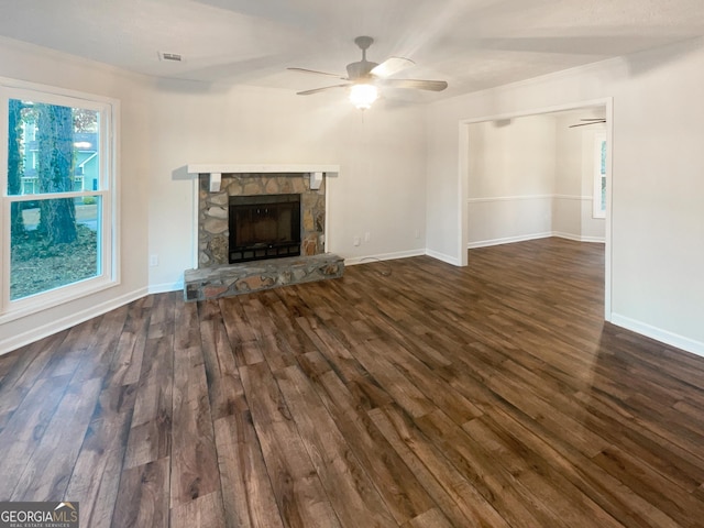 unfurnished living room featuring dark wood finished floors, a stone fireplace, baseboards, and a ceiling fan