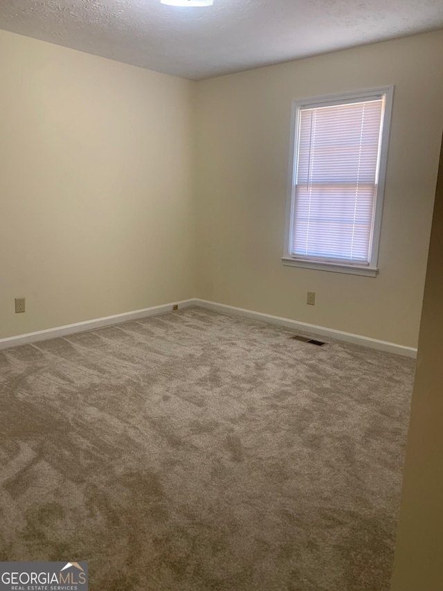 carpeted spare room featuring baseboards, visible vents, and a textured ceiling