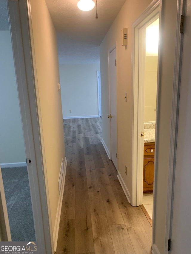 hallway featuring light wood finished floors, visible vents, and baseboards