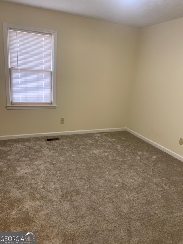 unfurnished room with carpet, visible vents, and baseboards