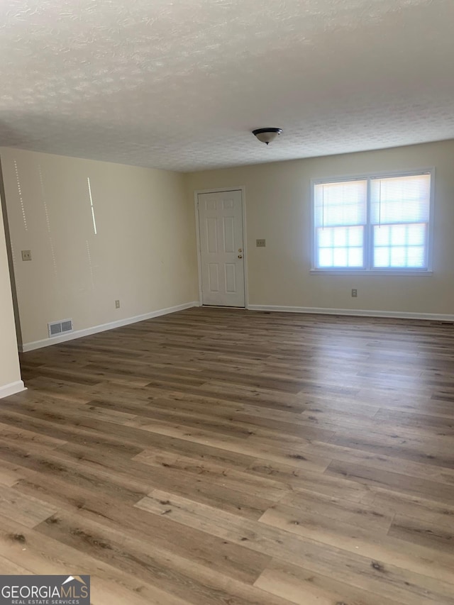 spare room with baseboards, wood finished floors, visible vents, and a textured ceiling