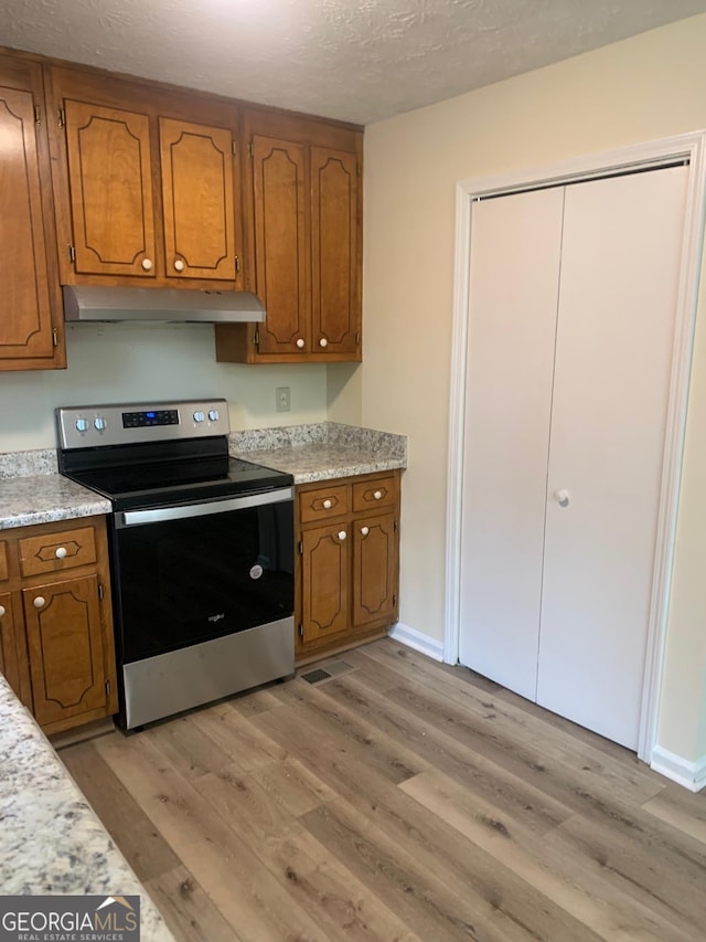 kitchen with under cabinet range hood, brown cabinets, stainless steel electric range oven, and light wood-type flooring