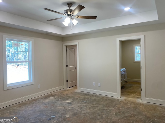 unfurnished bedroom featuring baseboards, unfinished concrete flooring, and a tray ceiling