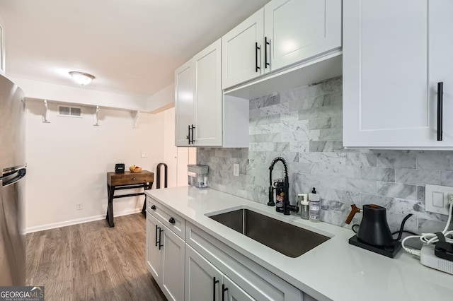 kitchen with a sink, wood finished floors, white cabinets, light countertops, and decorative backsplash