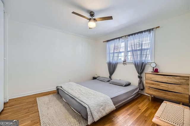 bedroom featuring crown molding, baseboards, wood-type flooring, and ceiling fan