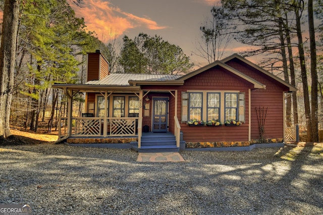 rustic home featuring a chimney, covered porch, and metal roof