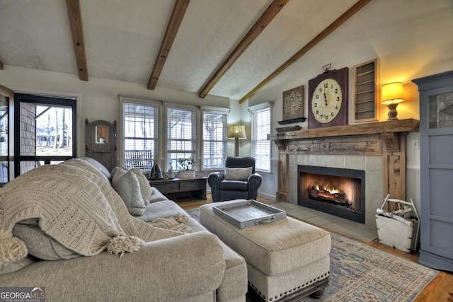 living room featuring a tiled fireplace, lofted ceiling with beams, and wood finished floors