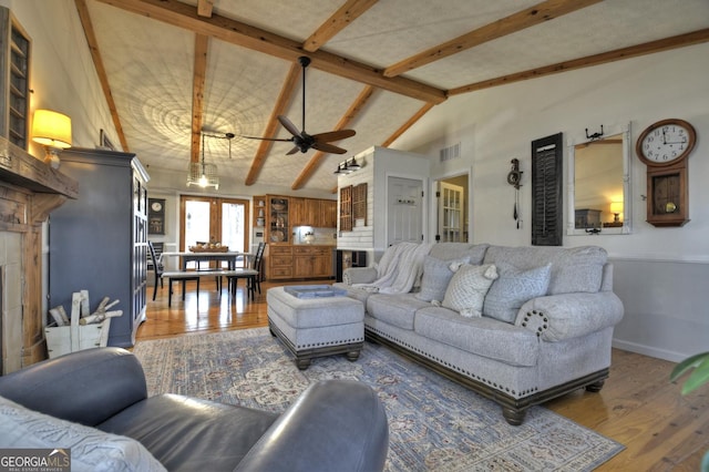 living room with lofted ceiling with beams, wood finished floors, visible vents, and baseboards