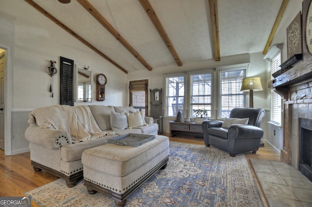 living room featuring beamed ceiling, a textured ceiling, wood finished floors, and a tile fireplace