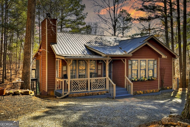 chalet / cabin featuring a standing seam roof, a porch, metal roof, and a chimney