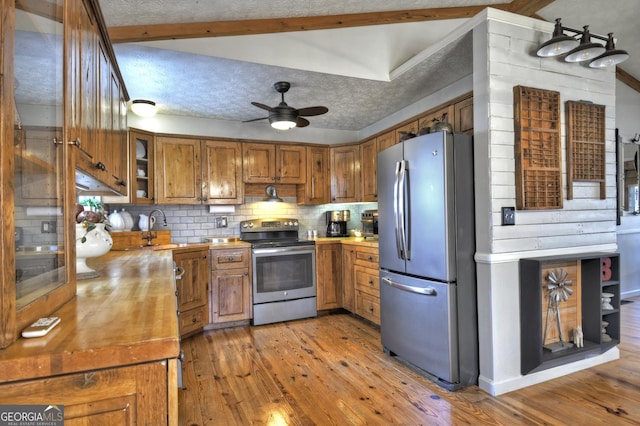 kitchen with brown cabinets, stainless steel appliances, a textured ceiling, tasteful backsplash, and light wood-type flooring