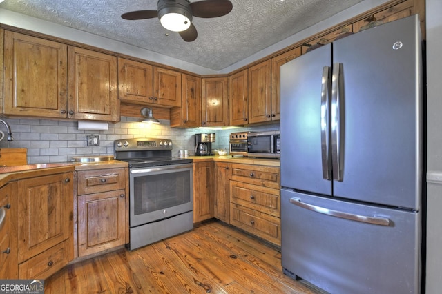 kitchen with a ceiling fan, dark wood finished floors, decorative backsplash, appliances with stainless steel finishes, and brown cabinets