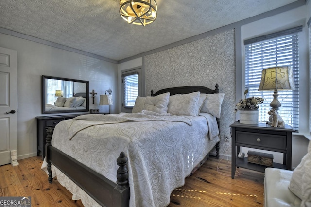 bedroom featuring a textured ceiling, wood finished floors, crown molding, wallpapered walls, and baseboards