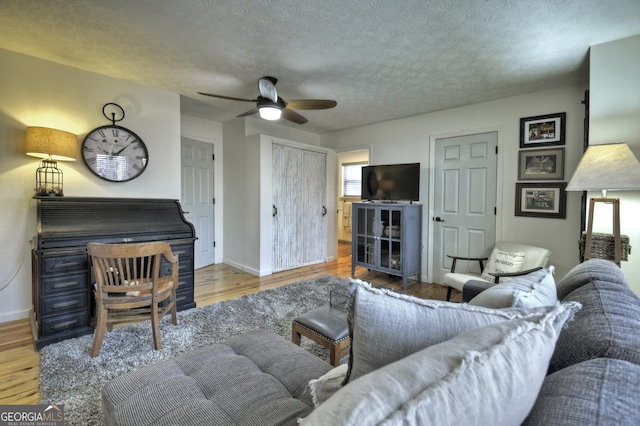 living room featuring a ceiling fan, wood finished floors, baseboards, and a textured ceiling