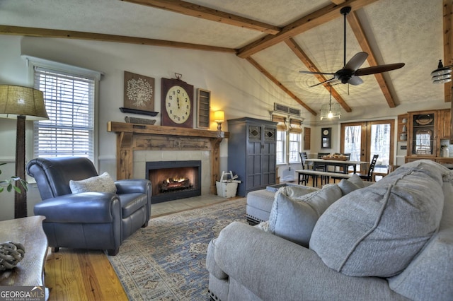 living area featuring ceiling fan, vaulted ceiling with beams, wood finished floors, and a tile fireplace