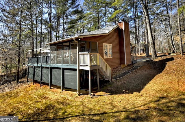 rear view of house with stairway, metal roof, a chimney, and a sunroom