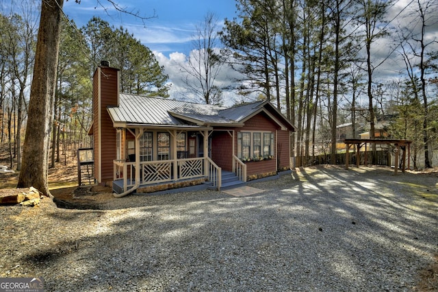 chalet / cabin featuring a standing seam roof, a porch, gravel driveway, metal roof, and a chimney