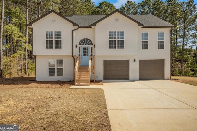 raised ranch featuring concrete driveway, a garage, and a shingled roof