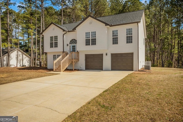 raised ranch with a front yard, driveway, roof with shingles, an attached garage, and central air condition unit