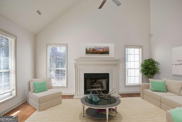 living area with a fireplace, wood finished floors, visible vents, and high vaulted ceiling