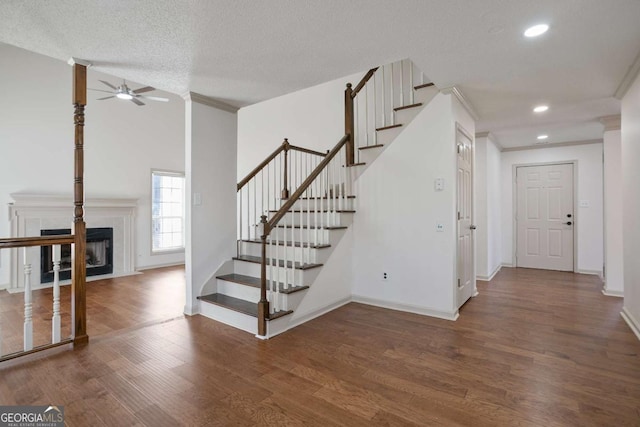 stairway with wood finished floors, baseboards, recessed lighting, a fireplace, and ornamental molding