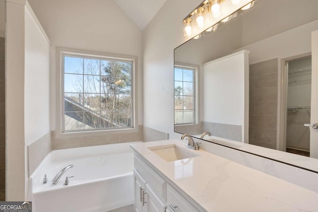 full bathroom featuring vanity, a walk in closet, a garden tub, and vaulted ceiling