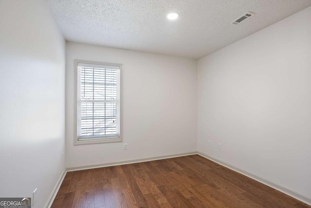 unfurnished room featuring visible vents, baseboards, a textured ceiling, and wood finished floors