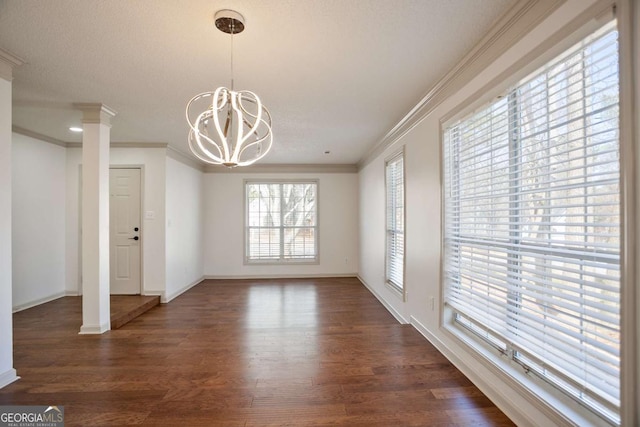 unfurnished dining area with baseboards, decorative columns, ornamental molding, dark wood-type flooring, and a chandelier