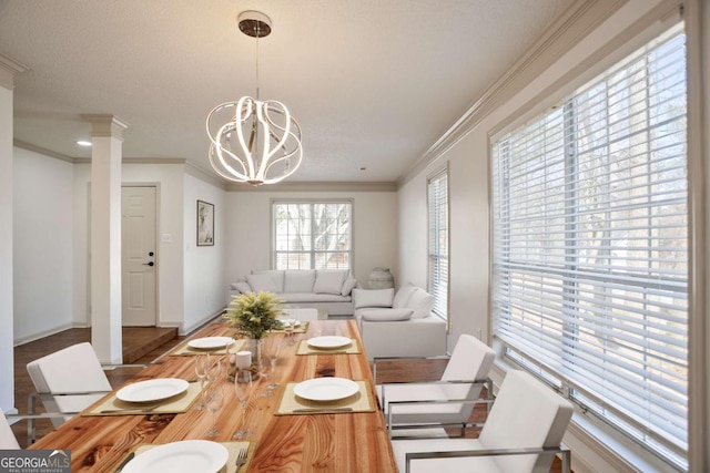 dining room featuring a chandelier, crown molding, baseboards, and decorative columns