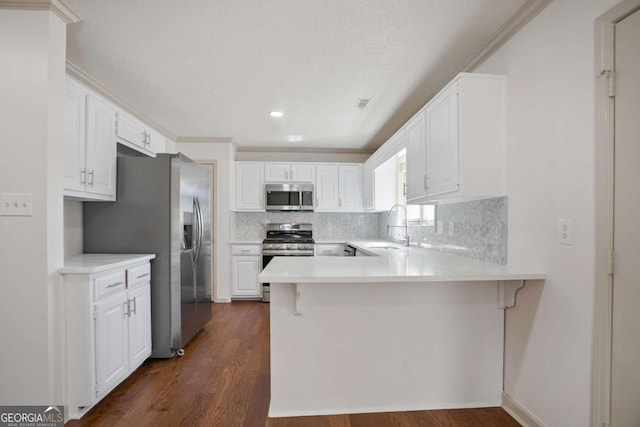 kitchen with a peninsula, a sink, light countertops, white cabinets, and appliances with stainless steel finishes