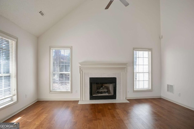 unfurnished living room featuring visible vents, high vaulted ceiling, wood finished floors, and a tiled fireplace