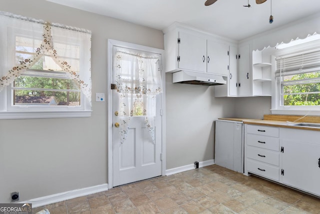 kitchen featuring under cabinet range hood, baseboards, plenty of natural light, and white cabinets