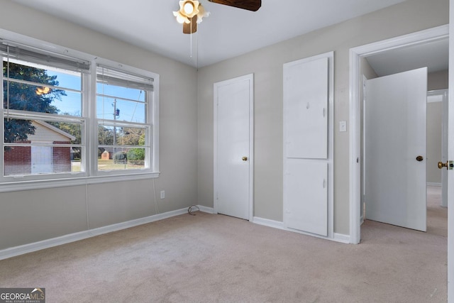 unfurnished bedroom featuring light colored carpet, a ceiling fan, and baseboards