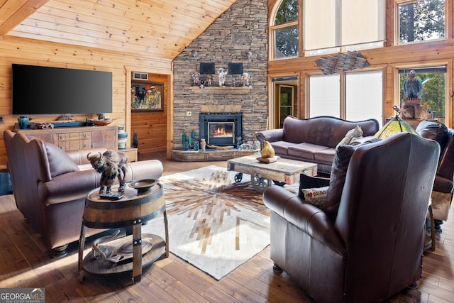 living room featuring high vaulted ceiling, hardwood / wood-style flooring, wooden walls, a stone fireplace, and wood ceiling