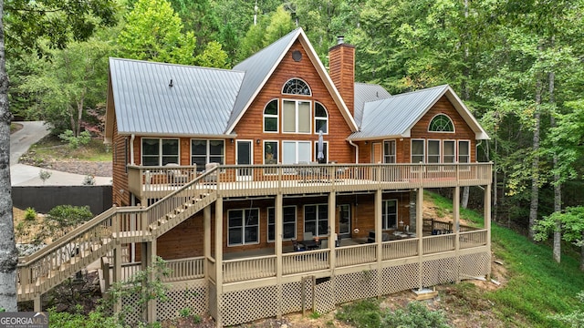 back of house featuring stairway, a wooded view, a chimney, and metal roof