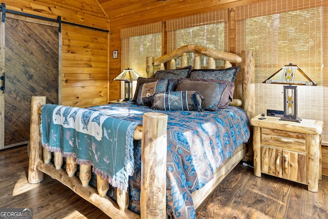 bedroom featuring a barn door, lofted ceiling, wooden walls, and wood finished floors